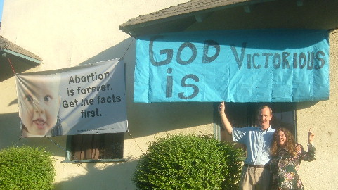 Terri and Tim point to 'God is Victorious' banner outside LifeHouse
